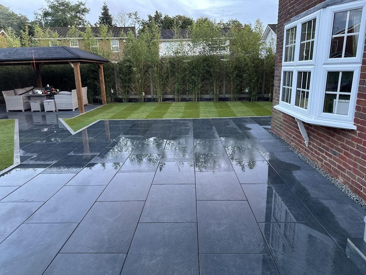 Dark grey porcelain paving laid around a house and lawn with a paved route to a covered seating area, completed by M&R Property & Paving Services
