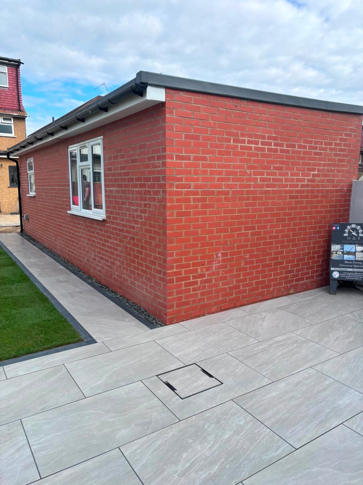 Completed garden landscaping by M&R Property & Paving Services with porcelain paving wrapping a brick extension beside new lawn