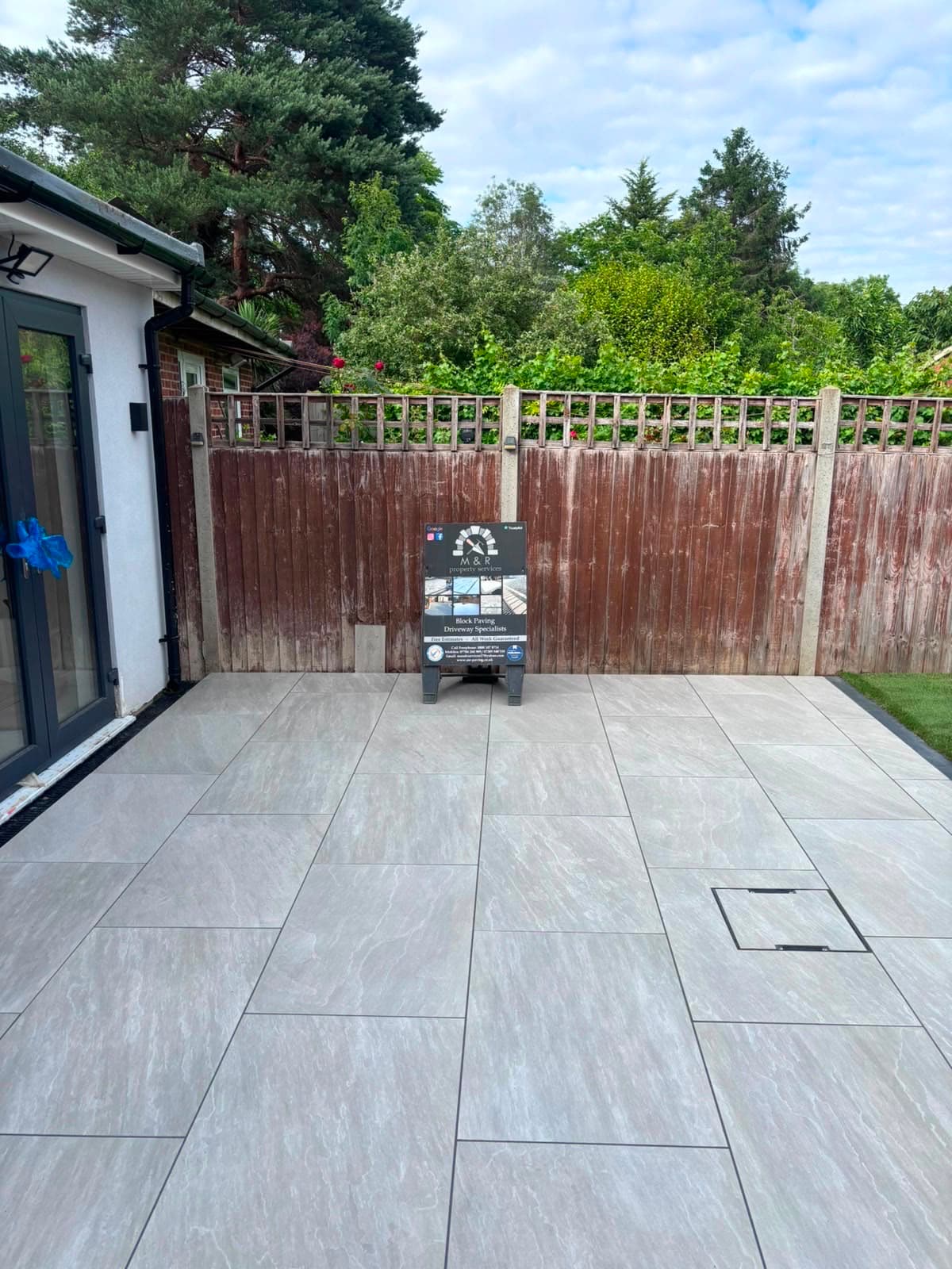 Enclosed courtyard rebuilt by M&R Property & Paving Services with pale porcelain paving and the company board against the fence