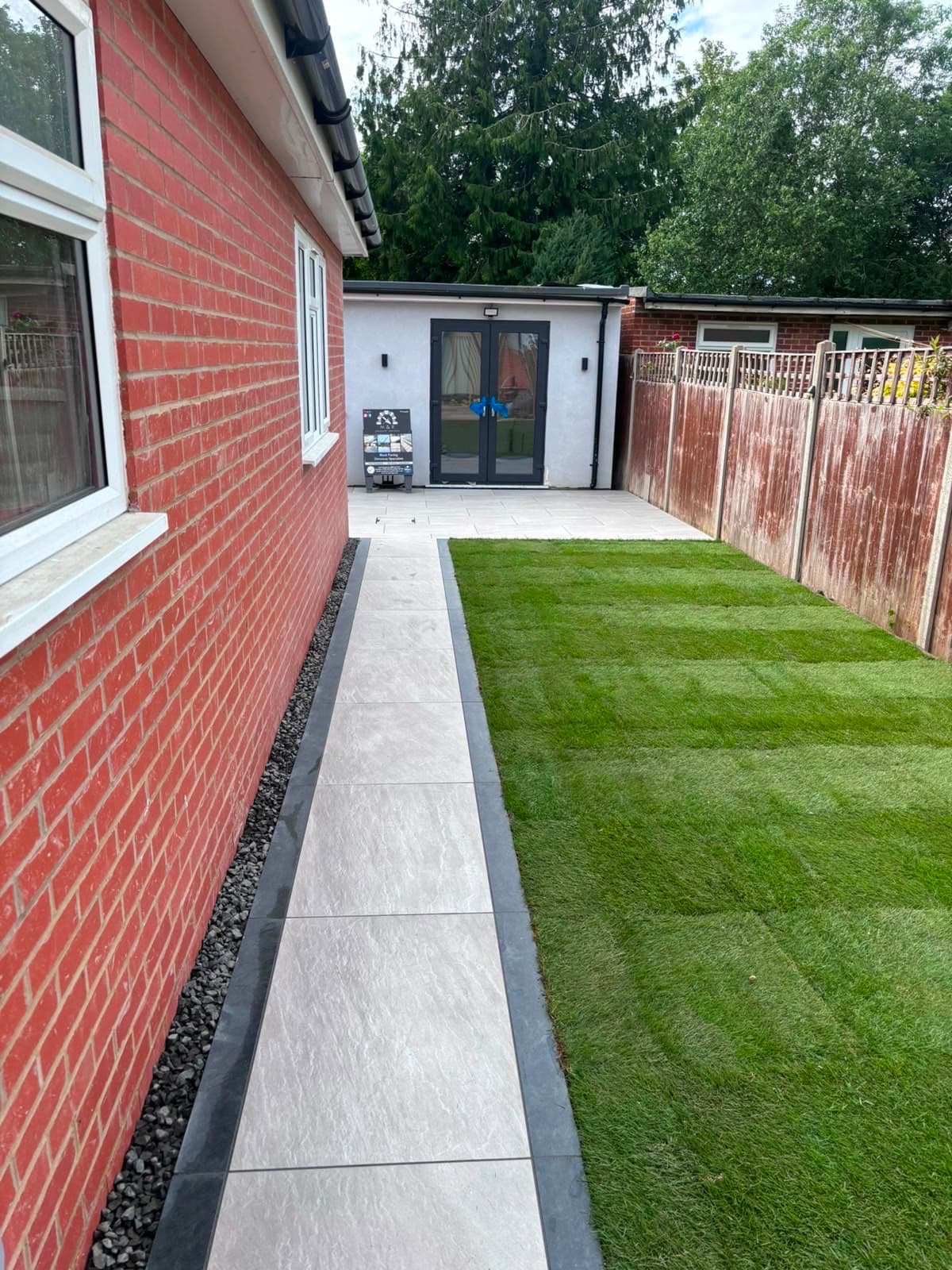 Porcelain garden pathway with charcoal border built by M&R Property & Paving Services beside new turf along a house wall