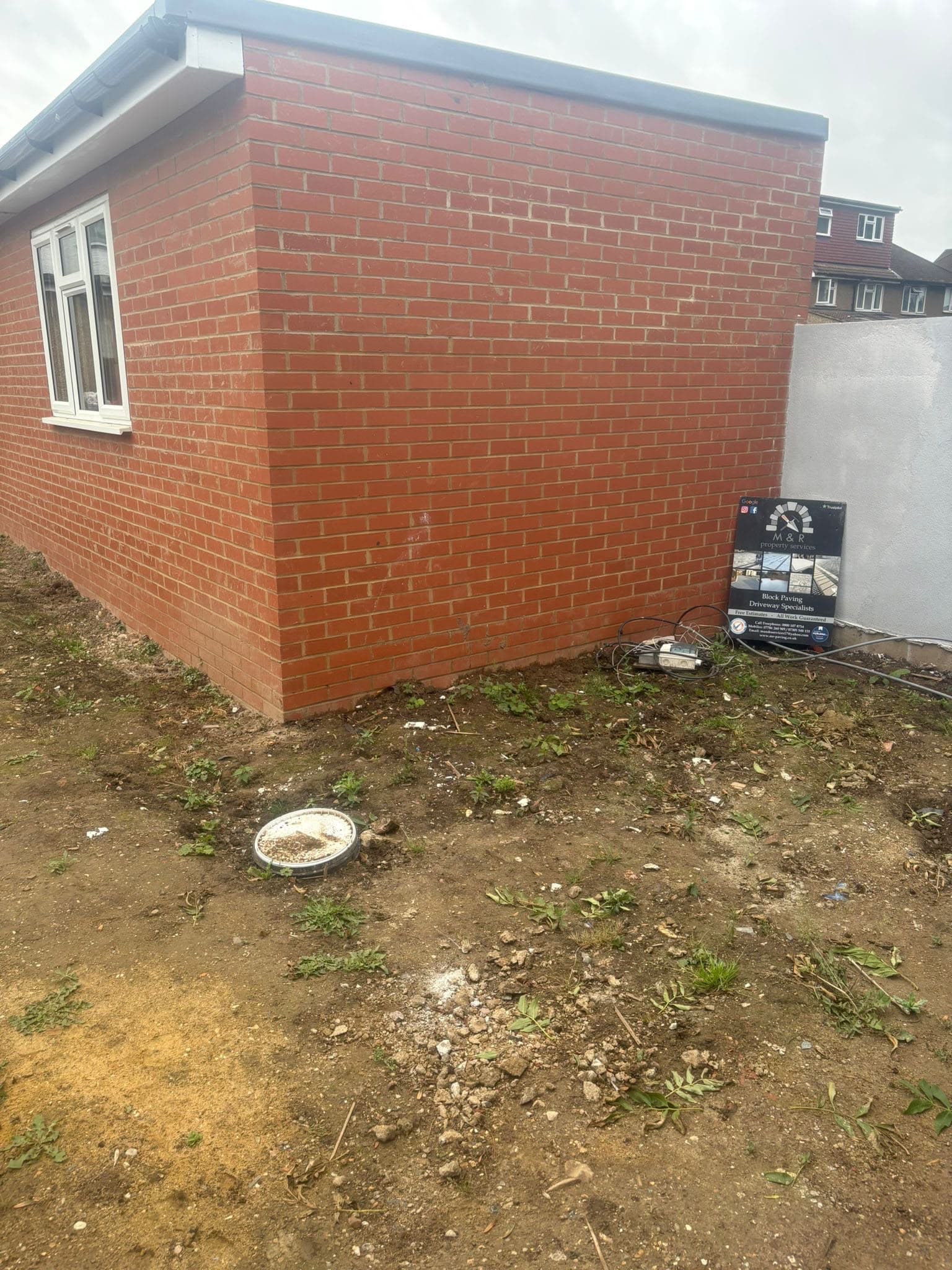Ground works underway beside a brick extension with the M&R Property & Paving Services board on site before paving