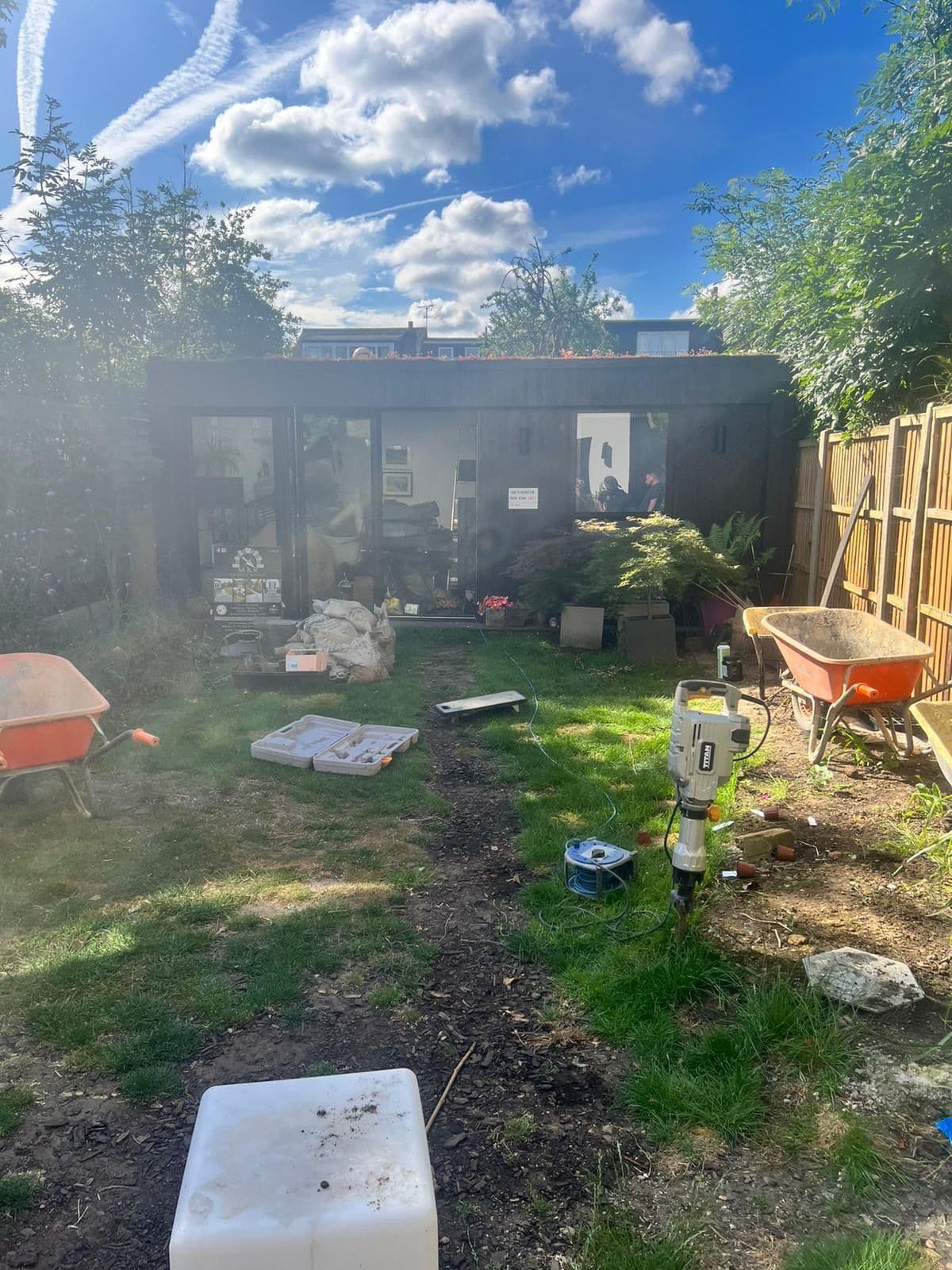 M&R Property & Paving Services mid-project in an established garden with tools and barrows working around a garden room and planting